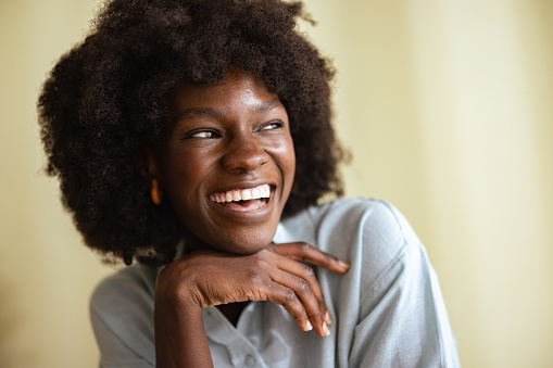 Portrait of a beautiful smiling carefree African American woman with afro hairstyle, looking away while holding her hand under her chin.