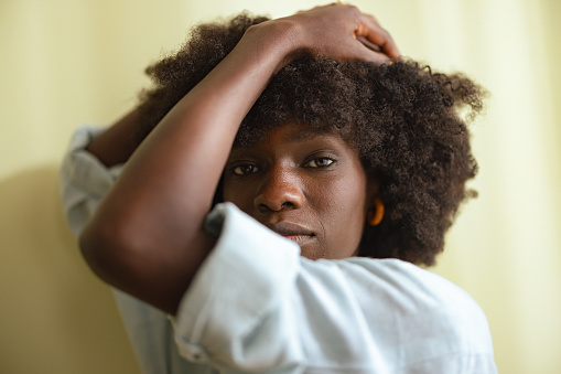 Close up shot of a beautiful serious African American Woman with afro hairstyle with her arms up holding her head and looking at the camera.