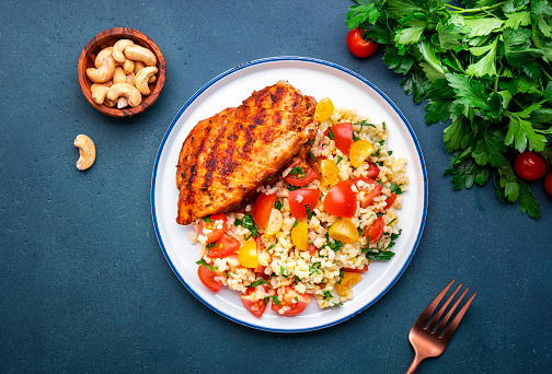 Grilled chicken with bulgur tabbouleh salad with tomatoes, parsley and olive oil and lemon dressing, blue stone table background, top view