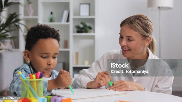 Adorable Little African American Boy With Curly Hair Having Fun At Pediatric Specialist Appointment Happy Child Drawing With Female Therapist Exercises For Children With Autism Stock Photo - Download Image Now
