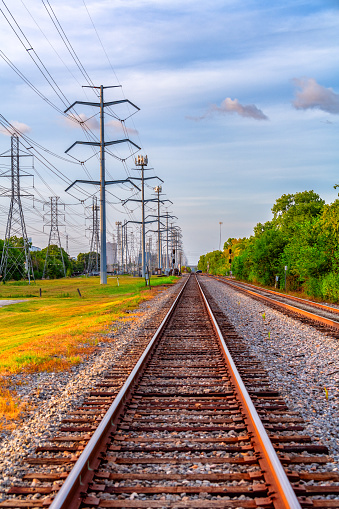 A set of railroad tracks flanked by a large array of high power electricity transmission lines bringing power to the Houston, Texas region.