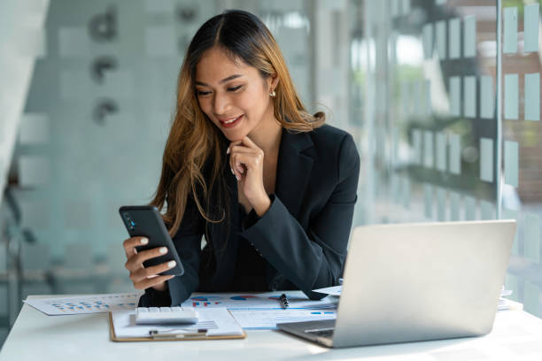 istock Young beautiful asian woman using smartphone and working with laptop while sitting at office desk, working from home concept. 1642323833