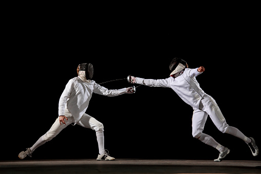 Two fencer in a fencing pose. One is attacking and one is defending. White on black background. Point.