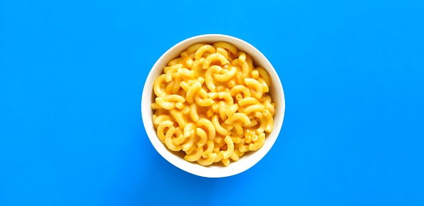 Macaroni and cheese in bowl over blue background with copy space. Top view, flat lay