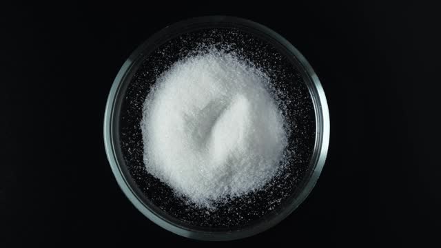 Trisodium citrate powder in Petri dish on dark background, top view. Food additive E331. Preservative and flavoring. Acidity regulator, emulsifier, complexing agent