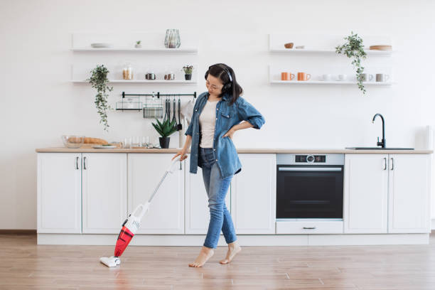 istock Asian lady using upright vacuum with music in headphones 1642378035