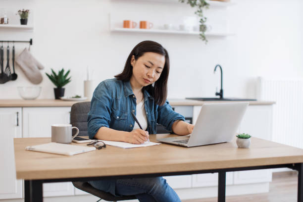 istock Adult writing down on paper while sitting behind laptop 1642380349