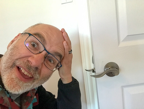 Headshot of mature mature with hand on head with deception expression because he wrongly installed a door know  so the door cannot close.