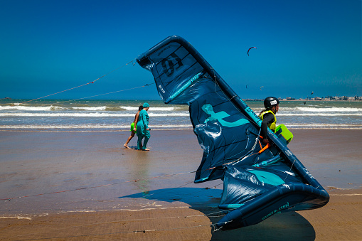 Essaouira, Morocco - August 3, 2023: A girl drags her kitesurfing kite on the beach. The place is renowned for lovers of this sailing sport, thanks to the strong wind which allows you to easily lift the kite in flight.