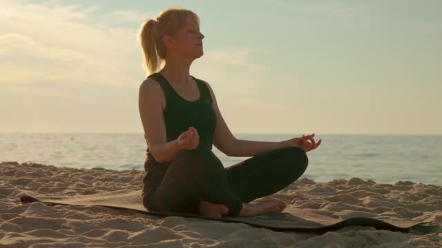 Adult woman doing yoga on sea beach outdoor. Sport exercises and mental health