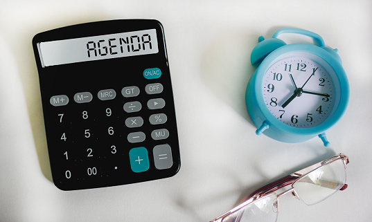 Agenda symbol. Calculator with word Agenda concept on white background with clock and glasses.