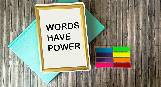 Notepad in a frame with text The words have power lying on a wooden background.