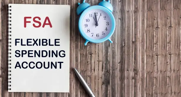Photo of FSA flexible expense account sign on notepad and wooden background