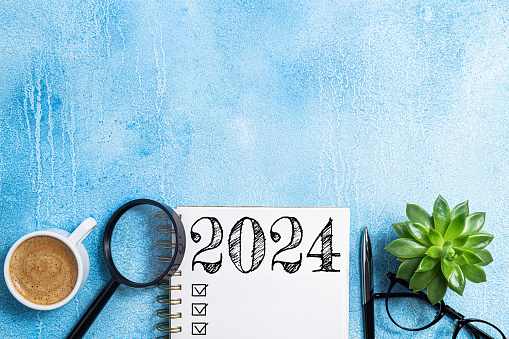 New year resolutions 2024 on desk. 2024 goals list with notebook, coffee cup, plant on blue table. Resolutions, plan, goals, action, checklist, idea concept. New Year 2024 resolutions, copy space