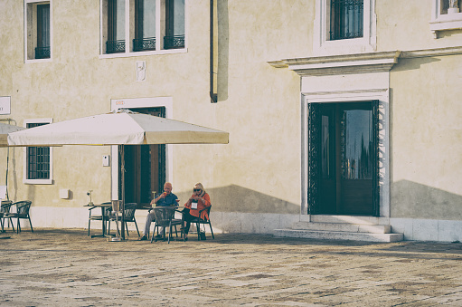 Venice, Italy - May 30 2023: Senior tourist couple at an outdoor restaurant cafe in Venice.. Picturesque idyllic scene