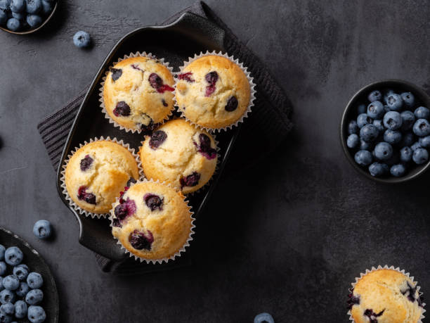 istock Beautiful blueberry muffins in black baking form with fresh blueberries on dark background. Culinary magazine cover. Postcard design. Elevated view. 1642537377
