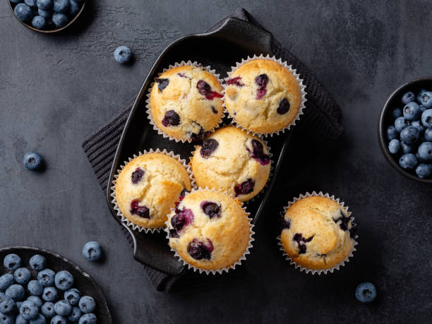 istock Beautiful blueberry muffins in black baking form with fresh blueberries on dark background. Culinary magazine cover. Postcard design. Elevated view. 1642537531