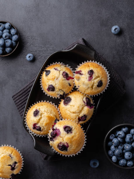 istock Beautiful blueberry muffins in black baking form with fresh blueberries on dark background. Culinary magazine cover. Postcard design. Elevated view. 1642538562