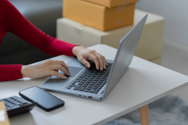 istock business owner SME, female entrepreneur using laptop to take and check online orders write customer information To prepare to pack boxes for sale and deliver to customers SME online business concept 1642543312