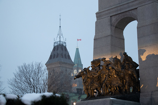 On a snowy afternoon, the National War Memorial in Canada's capital city, Ottawa, is seen lit. The Parliament Peace Tower in the far background.