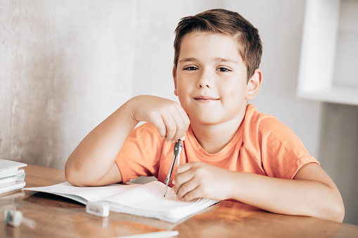 Little school boy doing homework with spring divider, sitting at the table