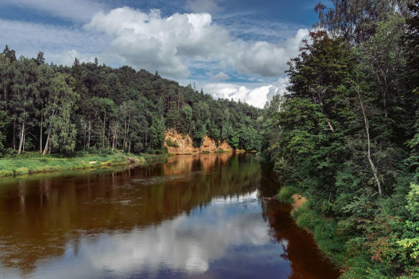 istock Landscape view of red sandstone Devil's cave cliffs(latvian: Velnalas klintis) on Gauja river in Sigulda, Latvia on a cloudy Agust day 1642595086