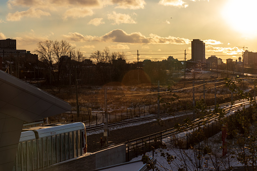 An OC Transpo light rail tram is seen at a station on the outskirts of downtown Ottawa, heading towards a bright sunset in Canada's capital city.