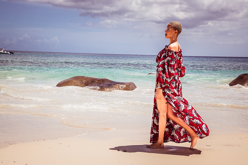 Beautiful Model enjoying fun and relaxing summer holiday by ocean and sea at Seychelles, East Africa, Smiling, happy and walking east African woman on a tropical vacation wearing the colorful dress- stock photo -Stock Photos