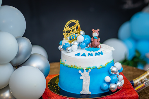 isolated one year birthday cake with white and blue balloons from different angle