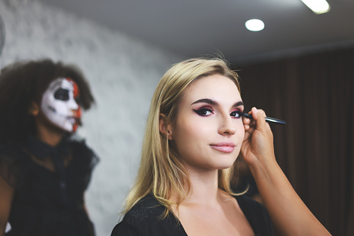 Makeup artist applying makeup for beautiful woman indoors in  Halloween concept. Close-up of a young artist woman while applying Halloween makeup