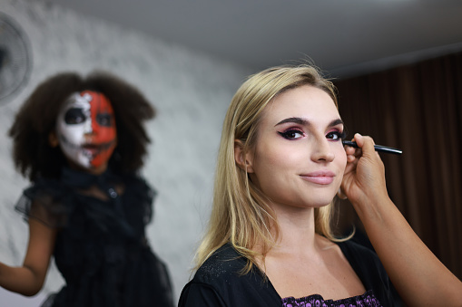 Makeup artist applying makeup for beautiful woman indoors in  Halloween concept. Close-up of a young artist woman while applying Halloween makeup