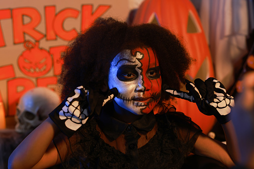 A little girl made up like the Day of the Dead indoors on Halloween night, Happy child with skull face paint celebrating Day of the Dead,  wide banner, copy space, Trick or Treat,