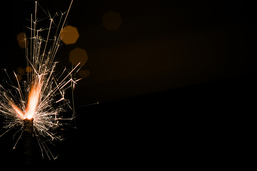 Burning sparkler in yellow and orange light on a black background. Closeup photo of Christmas and new year sparkler. Can be used like a wallpaper or postcard.
