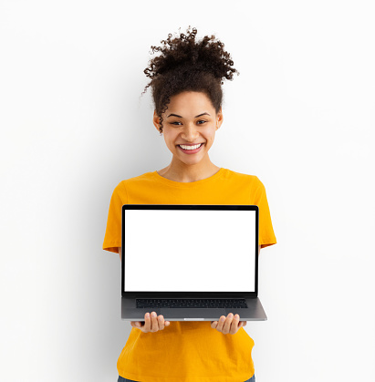 Happy smiling young African American woman holding laptop with blank screen standing on a white background