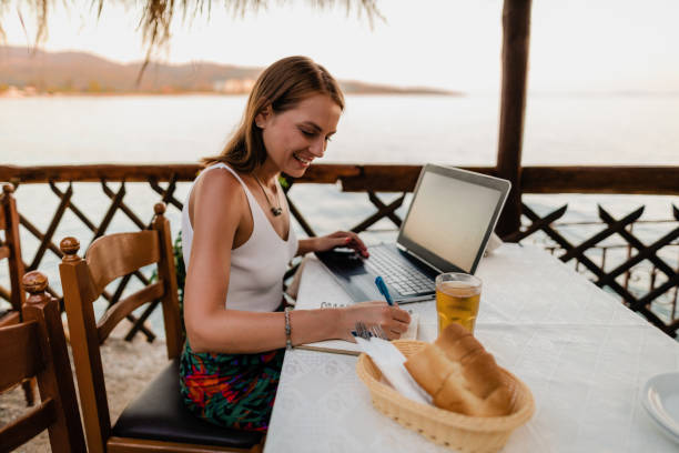 istock Smiling young woman writing and using a laptop in a seaside restaurant 1642783425
