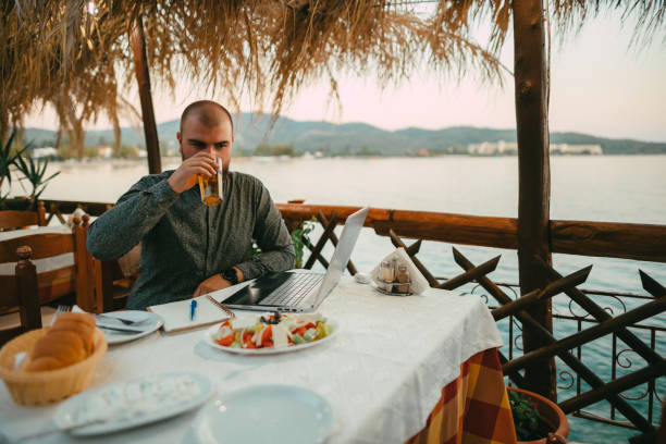 istock Young man writing and using a laptop in a seaside restaurant on a sunny summer day 1642783461