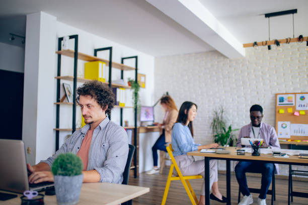 istock Businessman using laptop at modern office, her colleagues are working in the background 1642786122