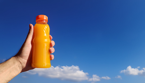 A bottle of freshly orange juice in hand on blue sky background