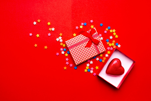 High angle view of Christmas gift box with sugar sprinkles of star shape over red color background.Conceptual mage about love in this season
