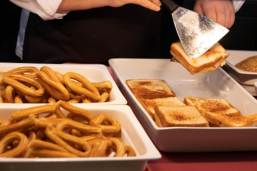 Unrecognizable woman serving sandwiches and churros ready to eat in a breakfast bufet in a resort hotel in Spain or Mexico