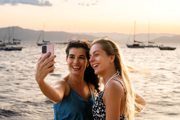 Beautiful women friends taking selfies against the background of the sea and yachts in Florianopolis Brazil Beautiful smiling two female friends taking a selfies using mobile phone against the background of the sea and yachts in Florianopolis Brazil yacht selfie stock pictures, royalty-free photos & images