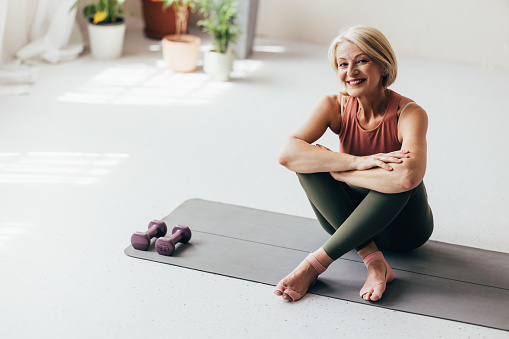 A portrait of a smiling Caucasian female in sports clothes sitting on her yoga mat after doing her daily workout.