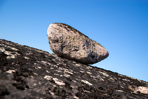 Large rock on a slope. Falling boulders. Clear blue sky background.