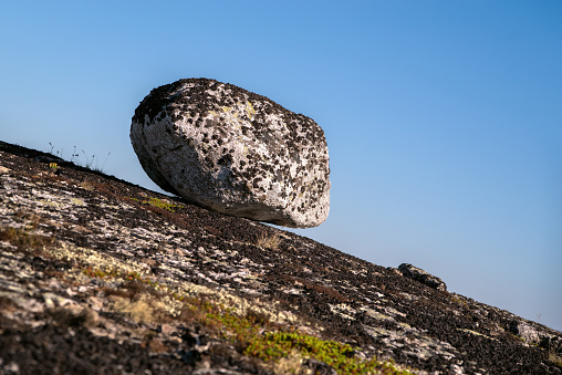 Large rock on a slope. Falling boulders. Clear blue sky background.