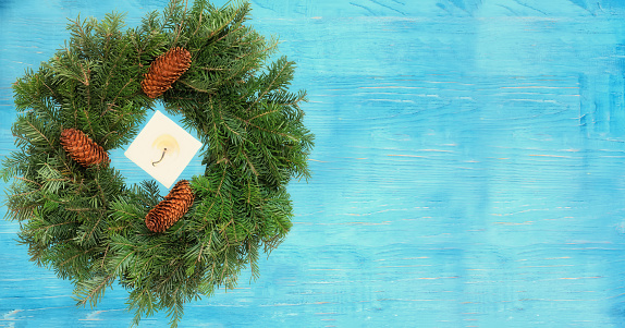 christmas wreath of fir branches and a candle on a blue wooden background. View from above. Banner. Free space for texts and your ideas.