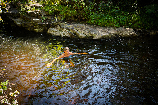 A mature woman enjoying the restorative power of nature.  She is wild swimming in a beautiful stream