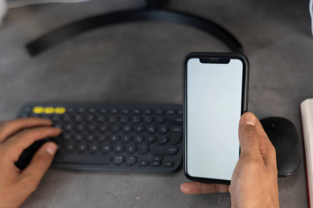 Top view mockup image of a man holding mobile phone with blank white desktop screen. Man using phone with white screen while lying on sofa at home , mock up screen.