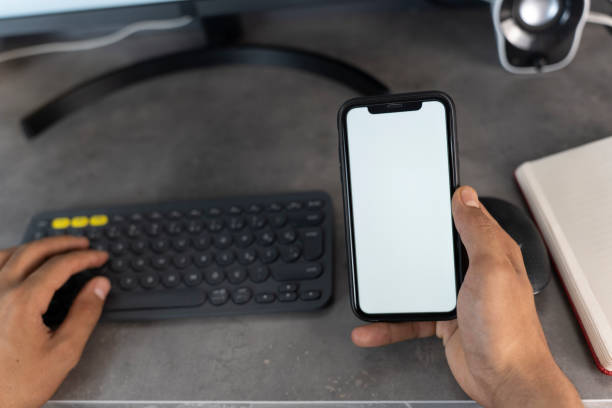 Top view mockup image of a man holding mobile phone with blank white desktop screen. Man using phone with white screen while lying on sofa at home , mock up screen.