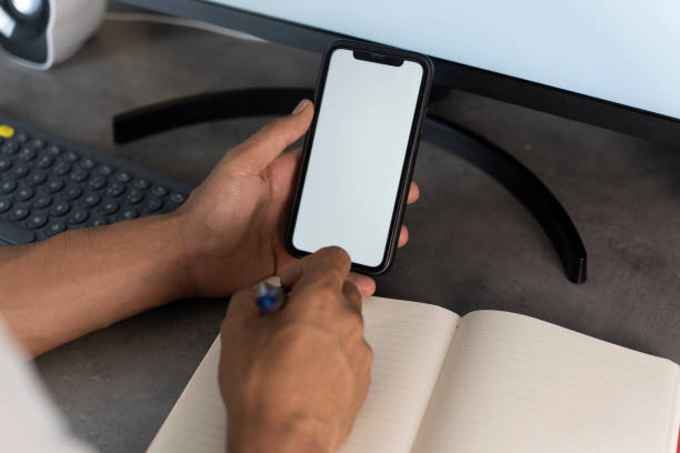 Top view mockup image of a man holding mobile phone with blank white desktop screen. Man using phone with white screen while lying on sofa at home , mock up screen.
