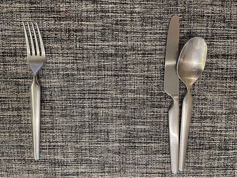 Spoons, forks, knives are placed on a wooden woven table mat.
